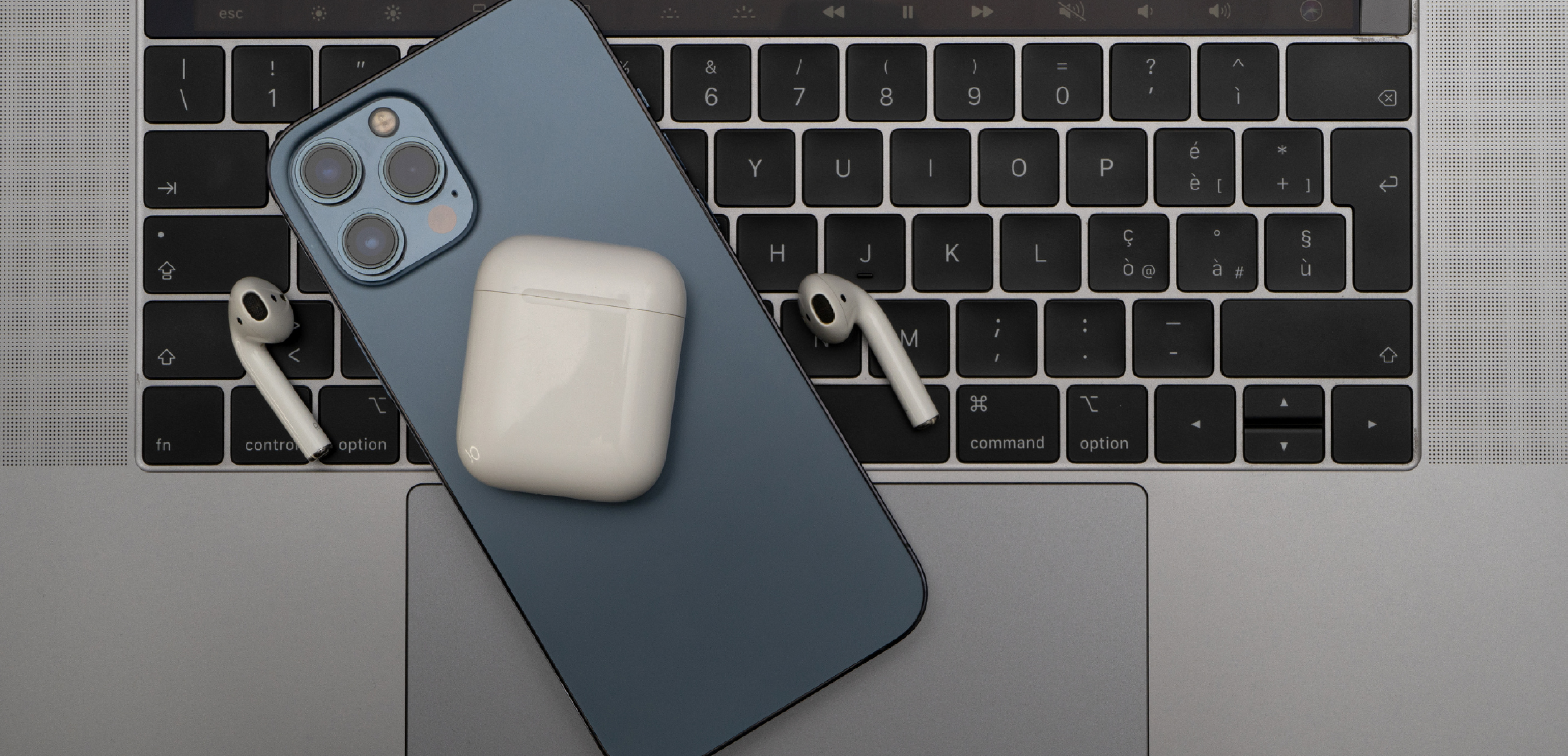 Photo of a grey MacBook keyboard with a navy blue iPhone and AirPods resting on top of it