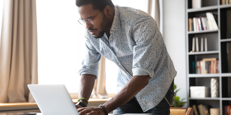 A handsome man in a floral button-up shirt hovers over a laptop. 